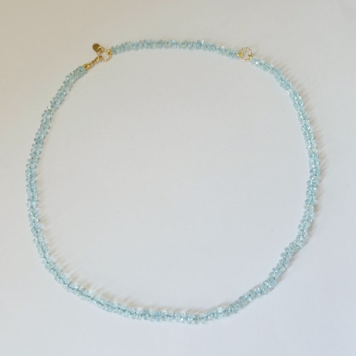 Flat lay view of a circular aquamarine bead necklace with solid 14K gold components.