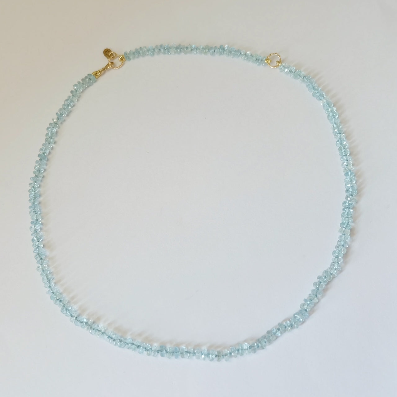 Flat lay view of a circular aquamarine candy necklace with solid 14K gold components.