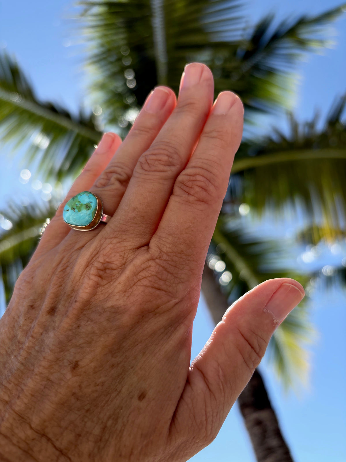 Woman's hand wearing a Sonora gold turquoise ring with sterling silver and gold rings