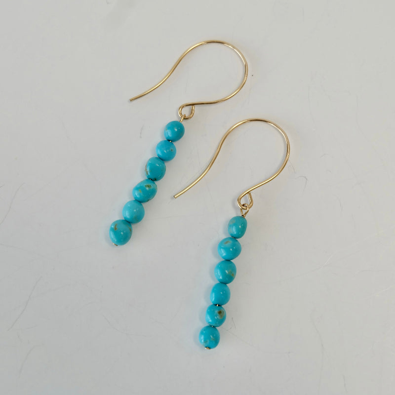 Turquoise 14k gold dangle earrings displayed on background.