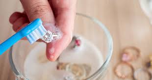 A small container of homemade jewelry cleaner next to a collection of gleaming rings and necklaces, highlighting their brilliance.