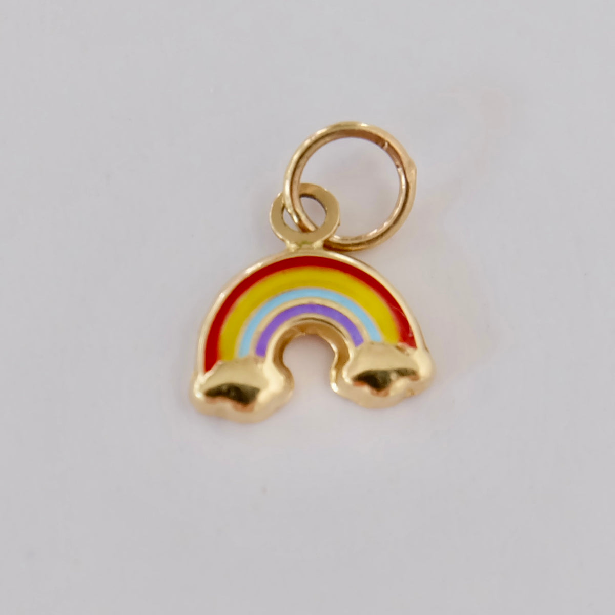 Close-up of a tiny 14K gold rainbow charm with colorful enamel