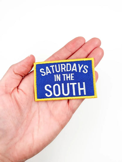 Blue patch with 'Saturdays in the South' text held in a hand against a white background