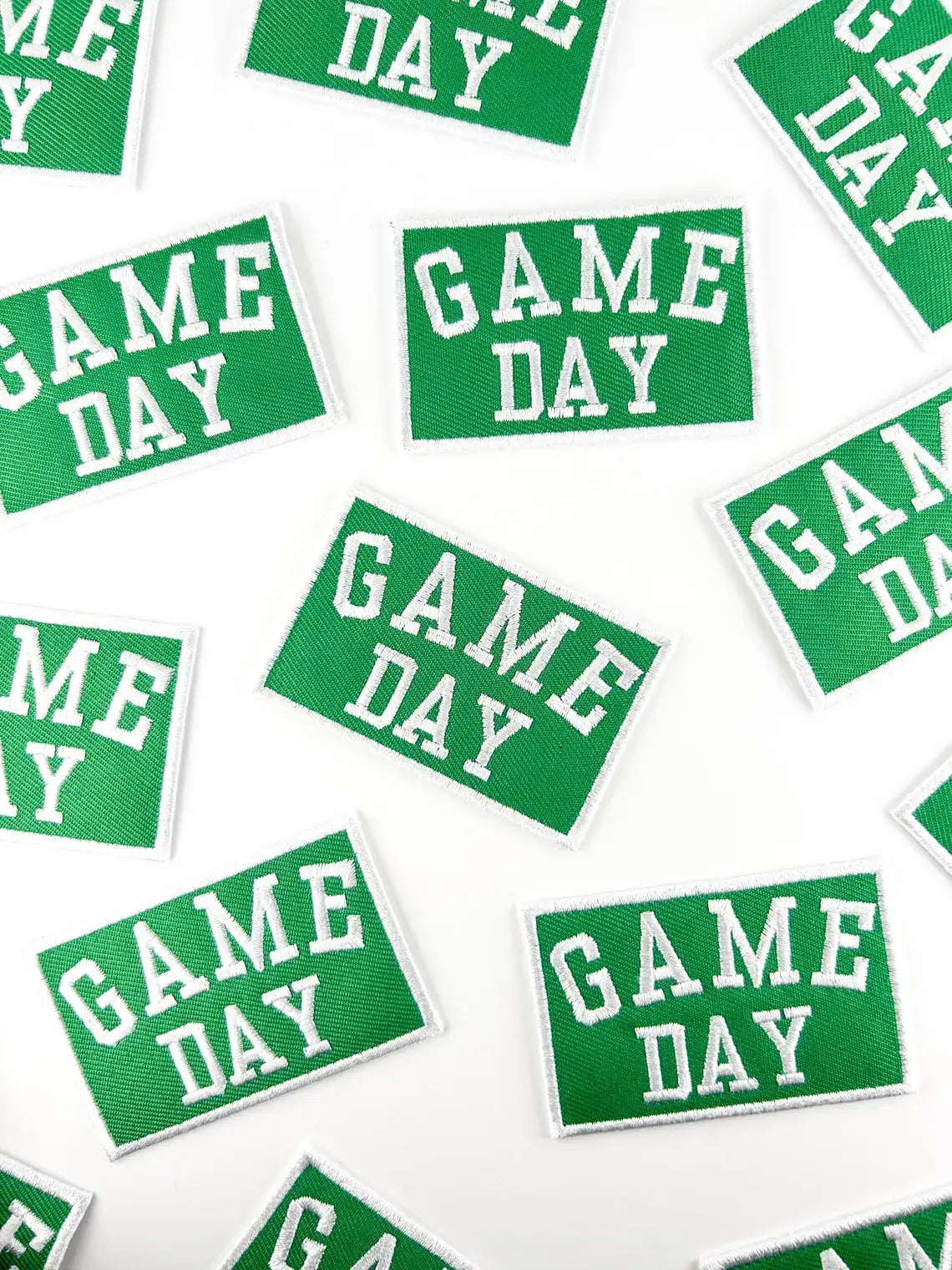 Green rectangular embroidered patches with white borders and the words 'GAME DAY' in white varsity-style lettering, scattered on a white background.