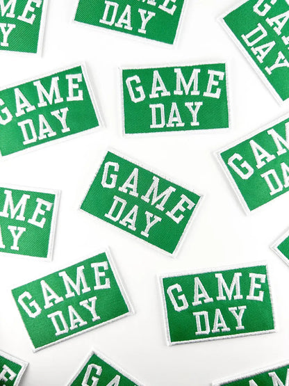 Green rectangular embroidered patches with white borders and the words 'GAME DAY' in white varsity-style lettering, scattered on a white background.