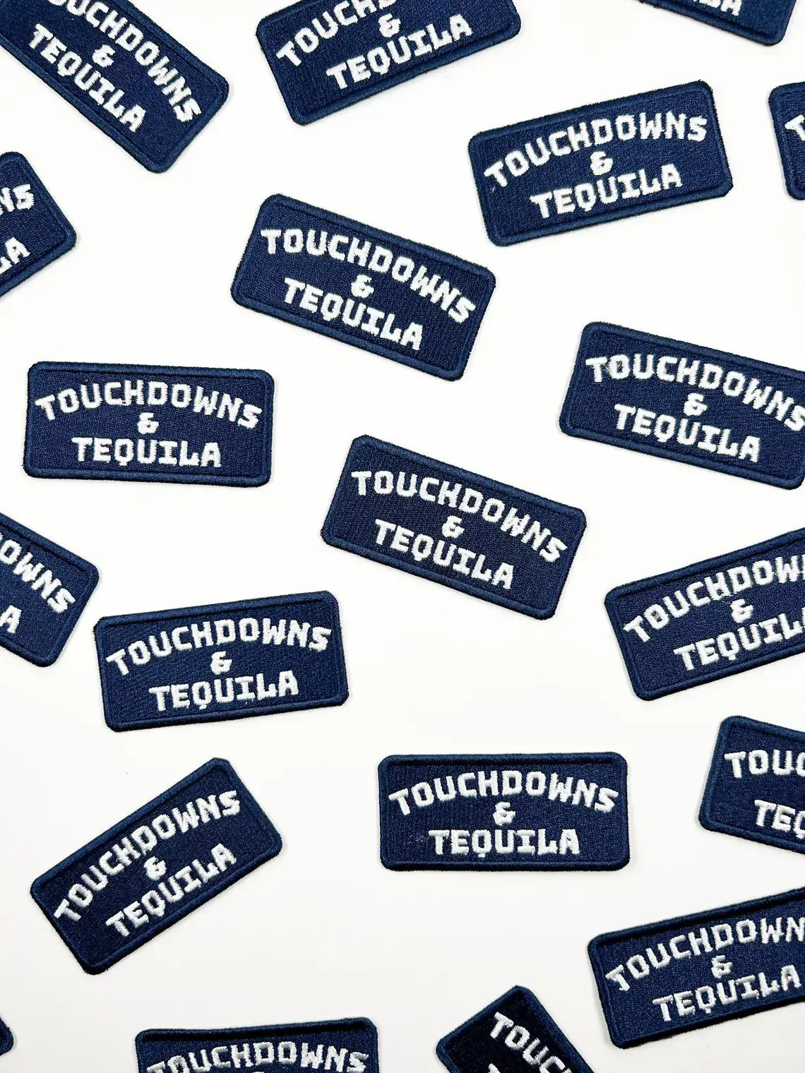 Multiple navy blue rectangular embroidered patches with white text reading 'TOUCHDOWNS & TEQUILA' scattered on a white background.
