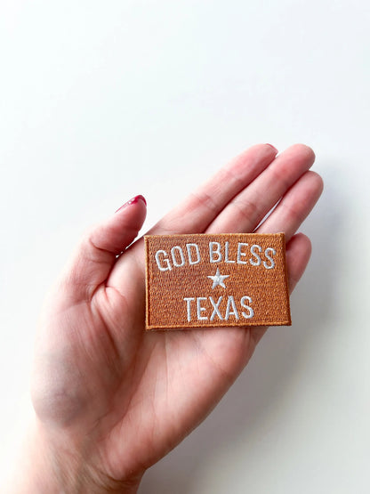 Hand holding a patch with 'God Bless Texas' text on a white background