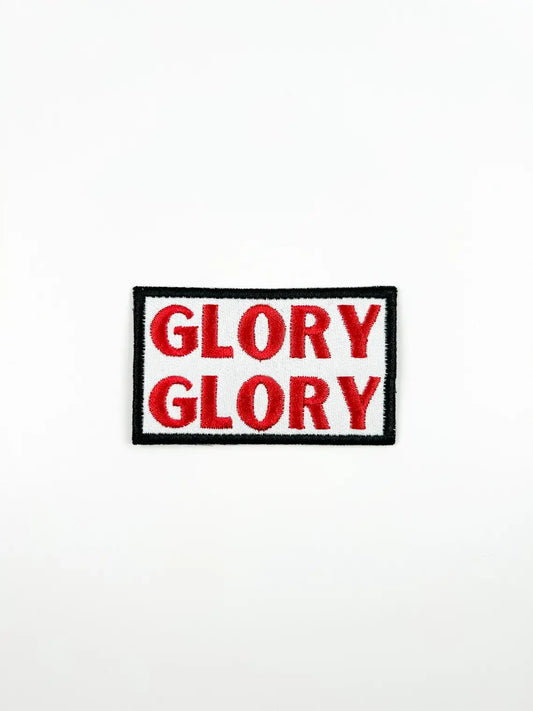 A rectangular embroidered patch with the word 'GLORY' repeated twice in red letters on a white background, bordered by black and white with a black outer border.