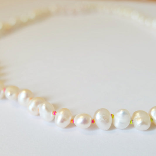 Close up of pearl necklace intricately knotted on colorful rainbow silk, highlighting the beauty of both materials.