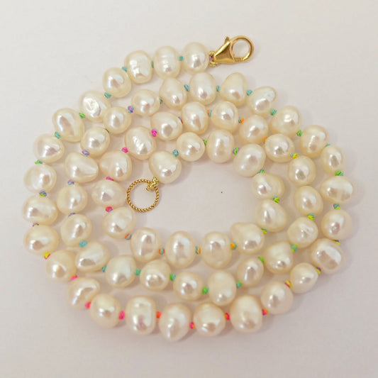 A pearl necklace elegantly knotted on vibrant rainbow silk, showcasing a blend of colors and classic elegance.