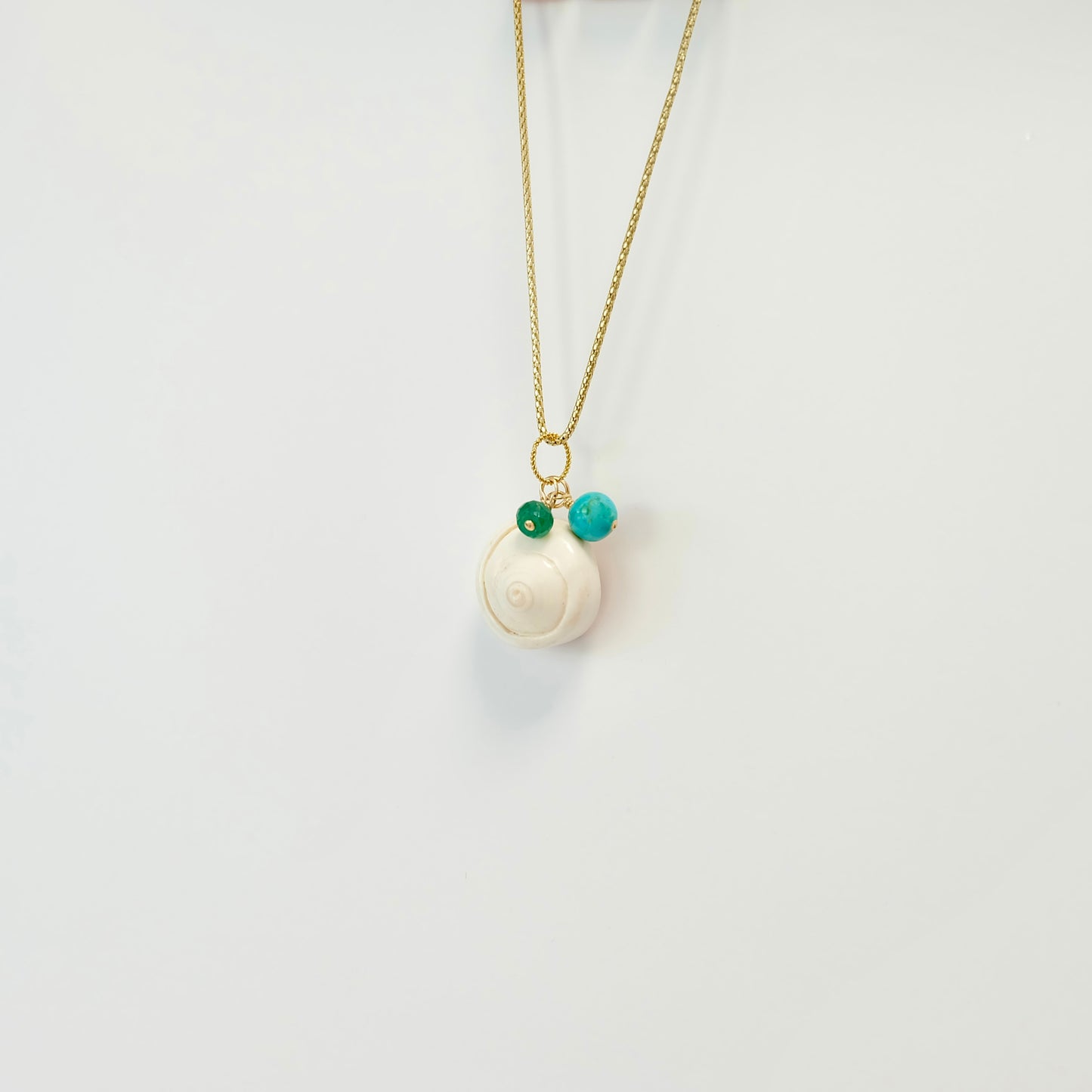 Turquoise sea shell charm featuring a sparkling emerald, ideal for enhancing your collection with a splash of coastal charm.