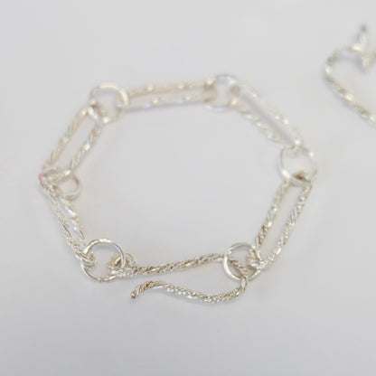 A sleek silver bracelet made of interconnected paperclip-shaped links, showcasing a modern and minimalist design.
