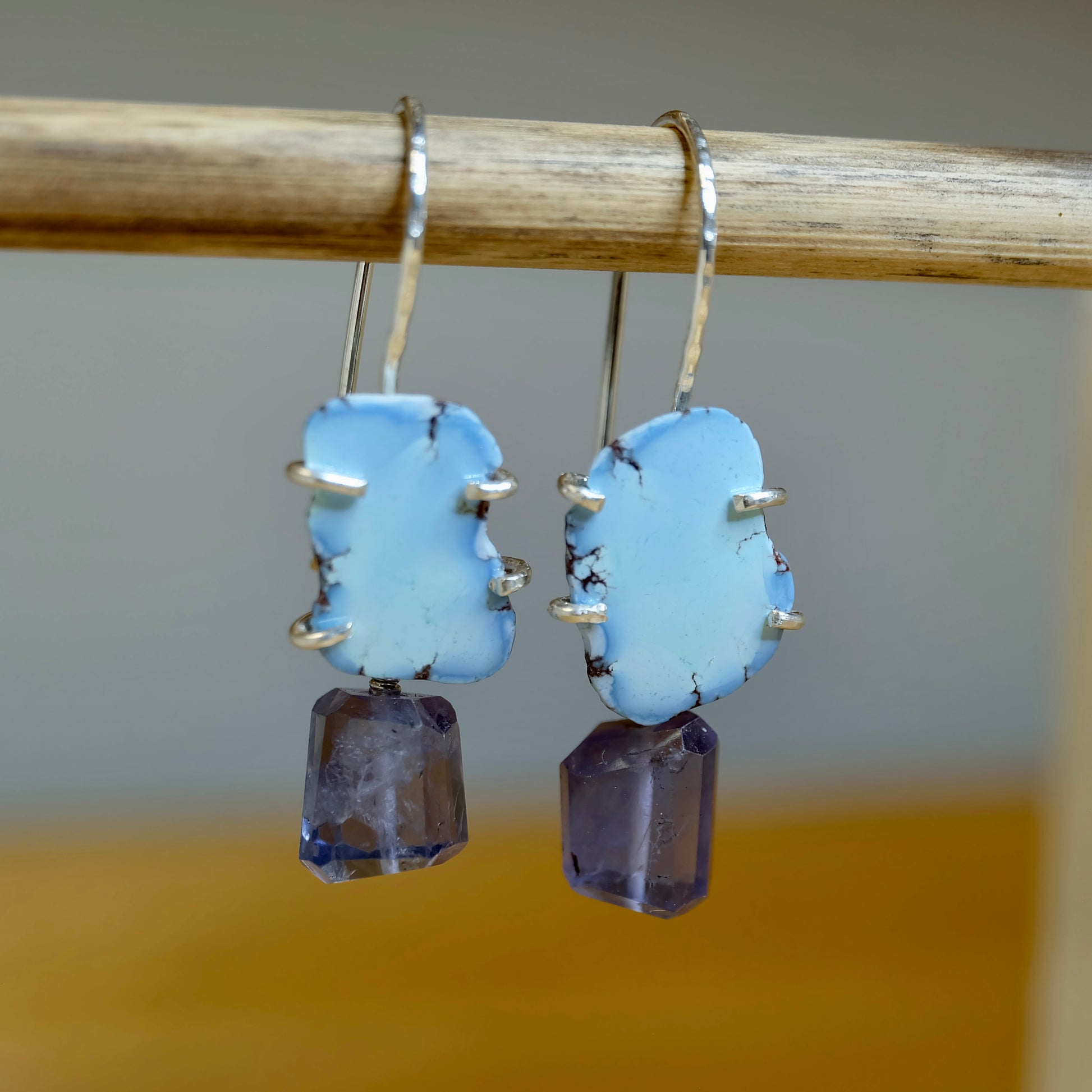 Iolite and Golden Hills turquoise dangle earrings in sterling silver displayed on a jewelry stand