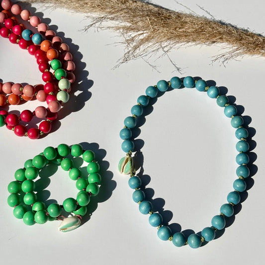 Three beaded necklaces in green, red, and blue on a white surface with a natural fiber background.