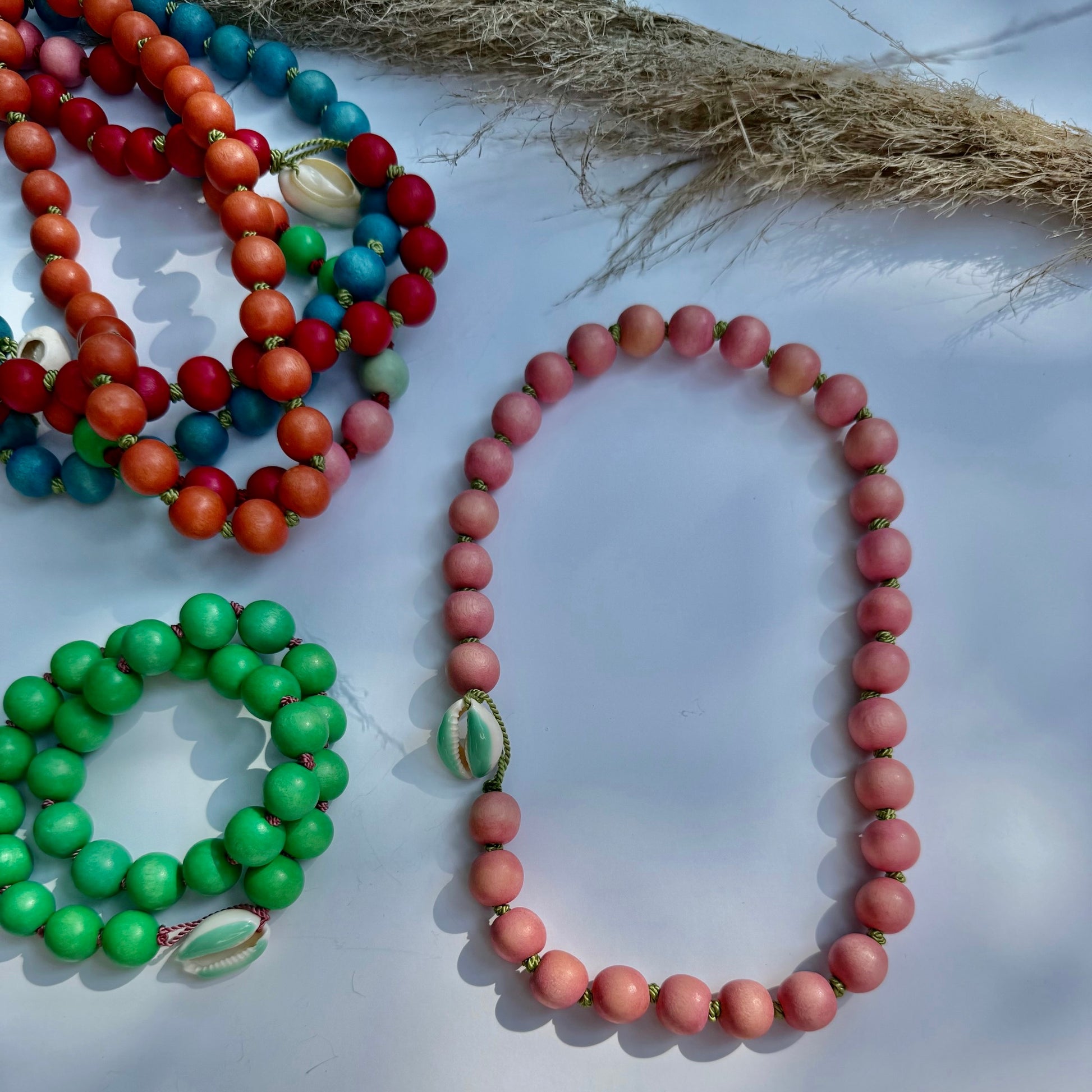 Colorful beaded necklaces on a white surface with a natural fiber rope.