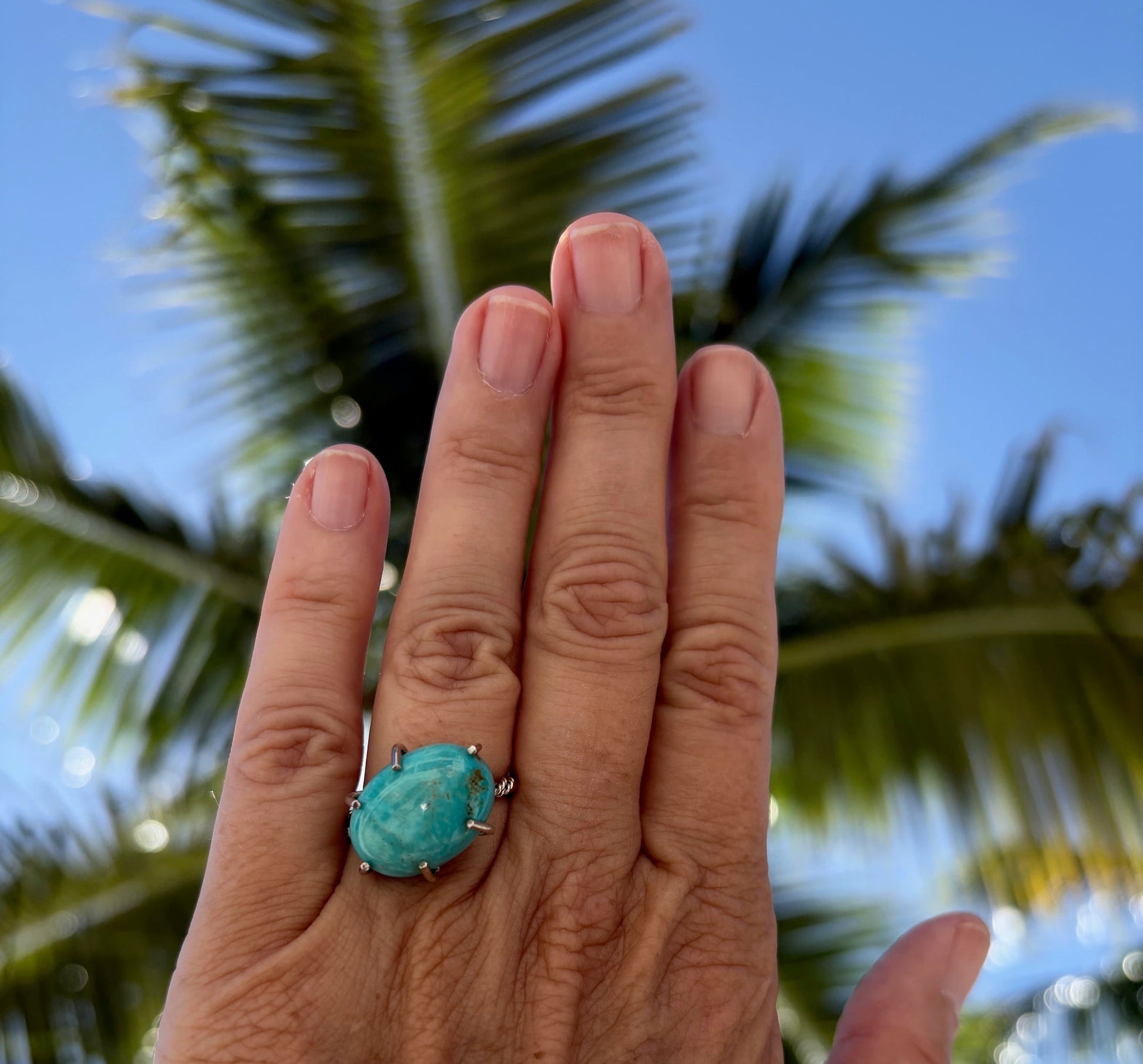 Woman's hand wearing a Kingman turquoise open prong ring.