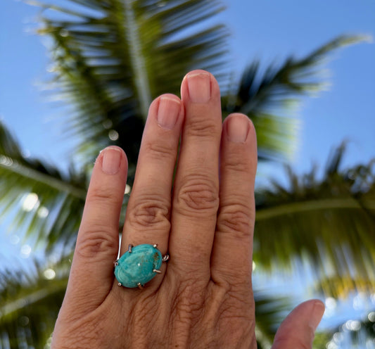 Woman's hand wearing a Kingman turquoise open prong ring.