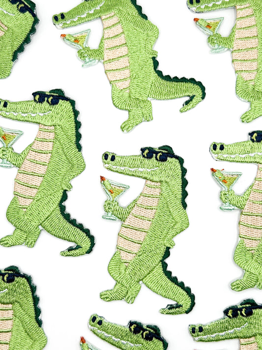 Alligator patch in green with tan belly and black sunglasses holding a cocktail