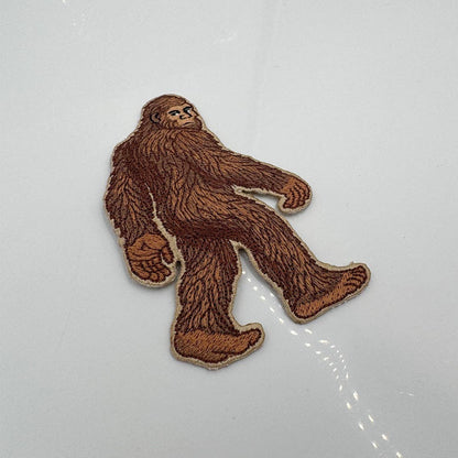 Embroidered patch of a brown Bigfoot-like creature on a white background