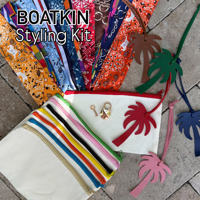 BOATKIN Styling Kit with colorful scarves, pouches, gold lock and key and palm tree bag charms on a stone surface.