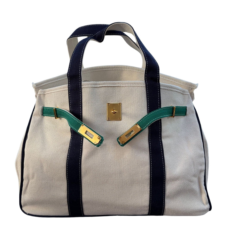 Side angle view of the cream canvas Boatkin boat tote bag displaying navy blue straps, forest green accents, and gold hardware clasp.