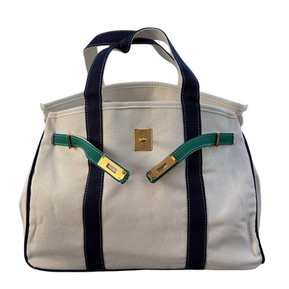 Side angle view of the cream canvas Boatkin boat tote bag displaying navy blue straps, forest green accents, and gold hardware clasp.