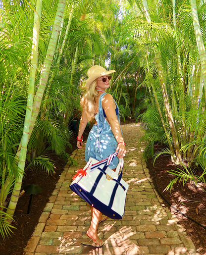 A girl walking with a navy blue boatkin surrounded by palm trees.