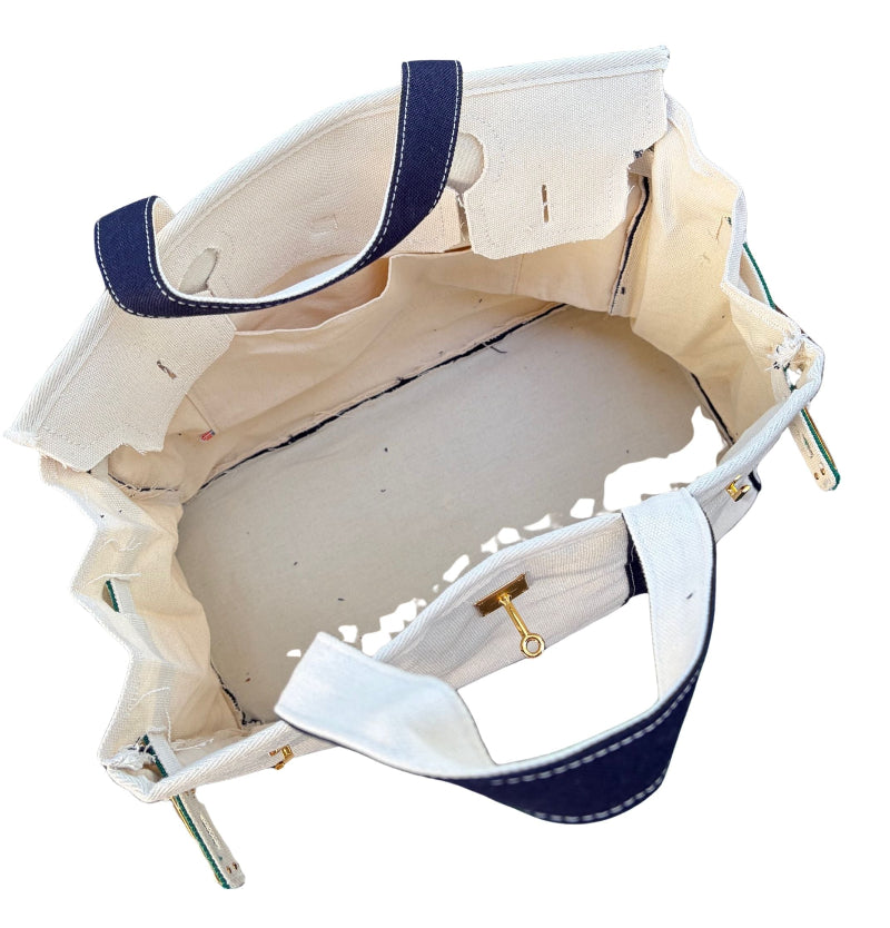 Close up angled look inside an open cream canvas Boatkin tote bag showing the light blue liner and gold hardware hook.