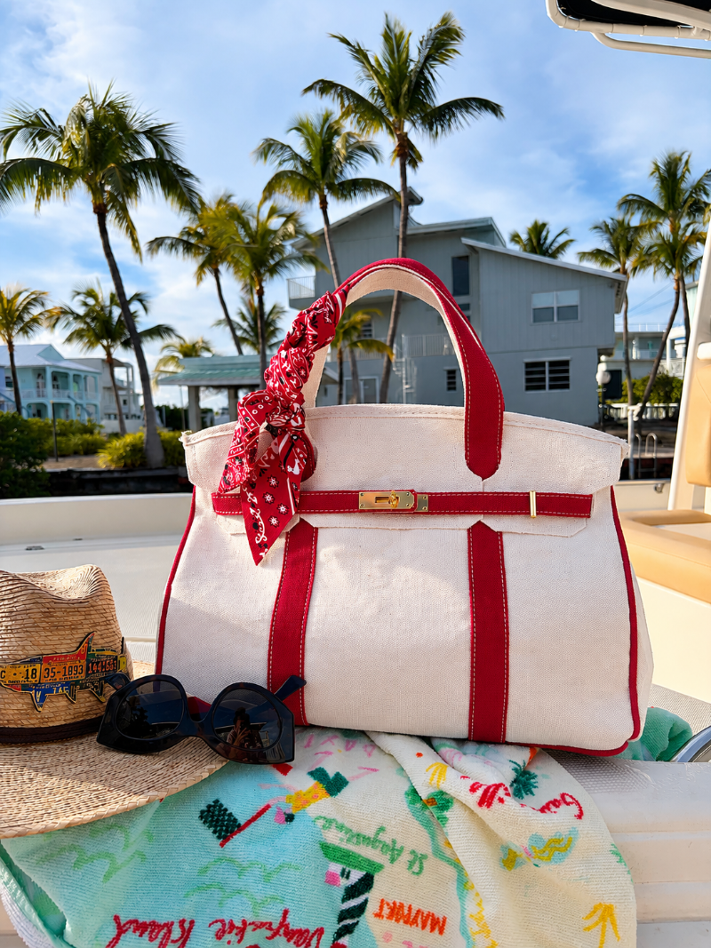 Boatkin tote bag with red straps on a boat with palm trees and buildings in the background