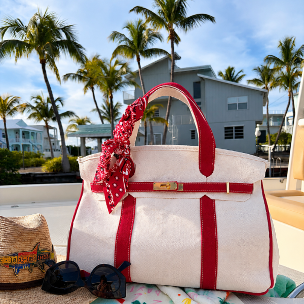 Boatkin tote bag with red straps on a boat with palm trees and buildings in the background