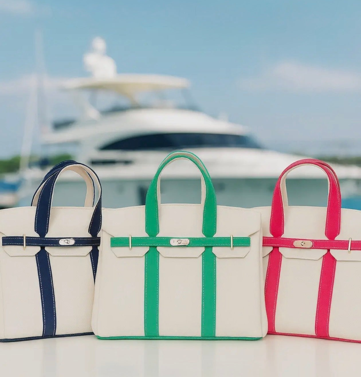 Three Boatkin tote bags with colorful straps on a boat deck with a blurred yacht in the background.