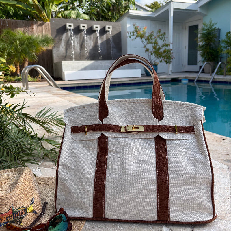 Brown Boatkin tote by a pool with a house and palm trees in the background.