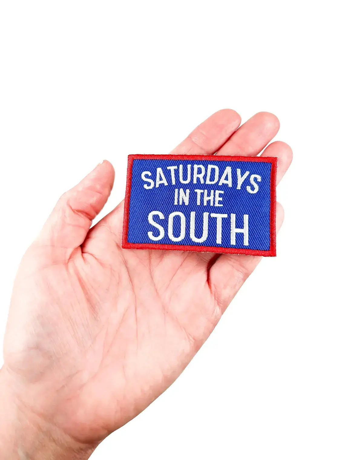 Hand holding a patch with 'Saturdays in the South' text on a white background