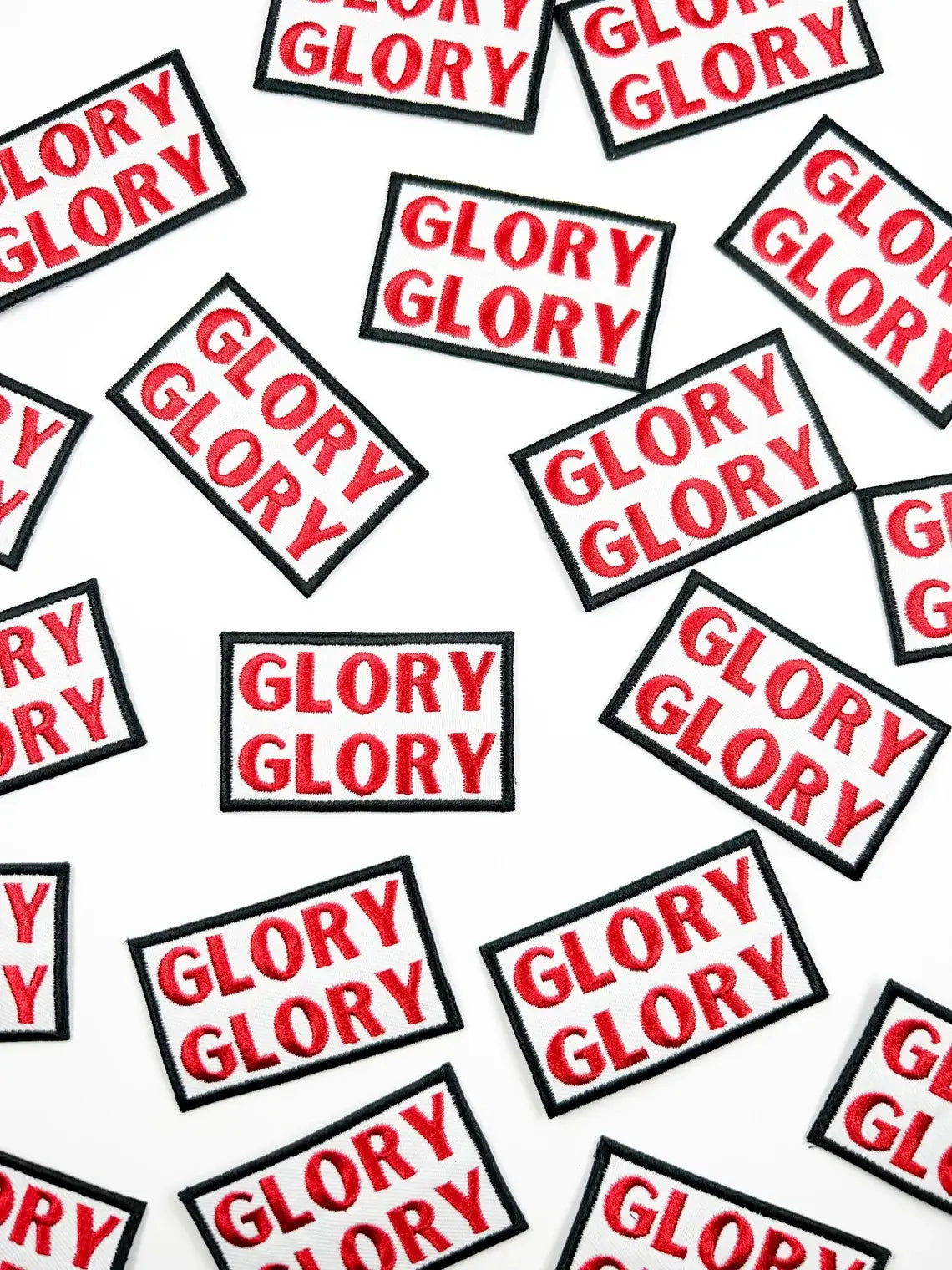 Multiple rectangular embroidered patches with the word 'GLORY' repeated in red text on a white background, each outlined with a black border, scattered across a white surface.