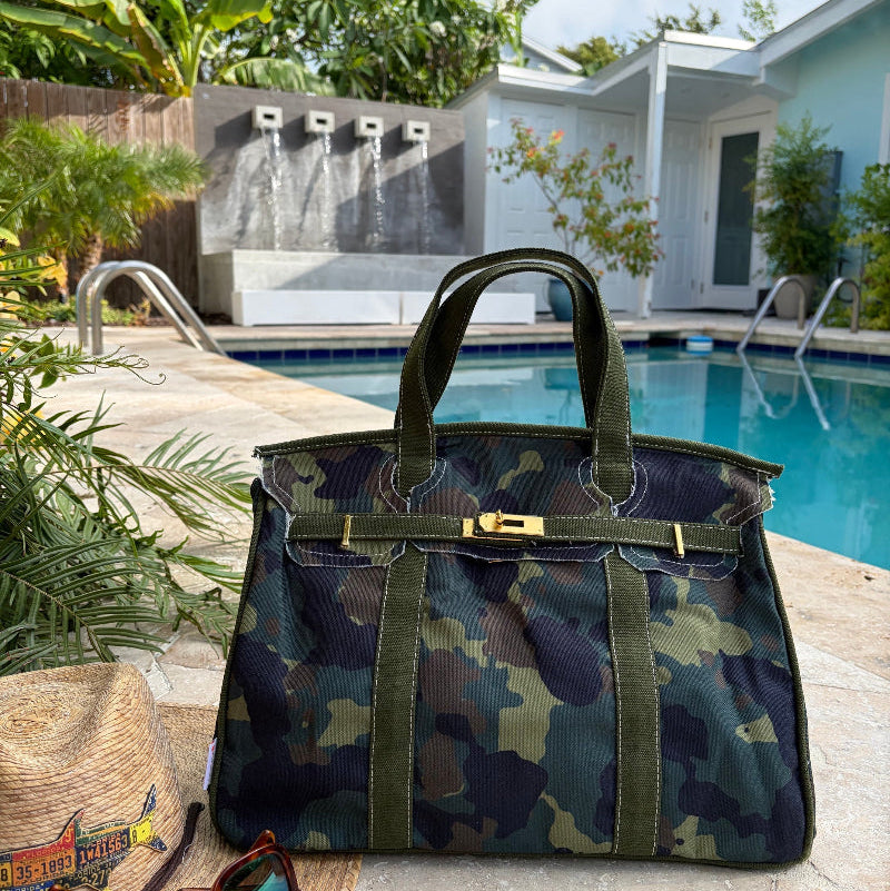 Camoflage Boatkin bag by a pool with a house and palm trees in the background.
