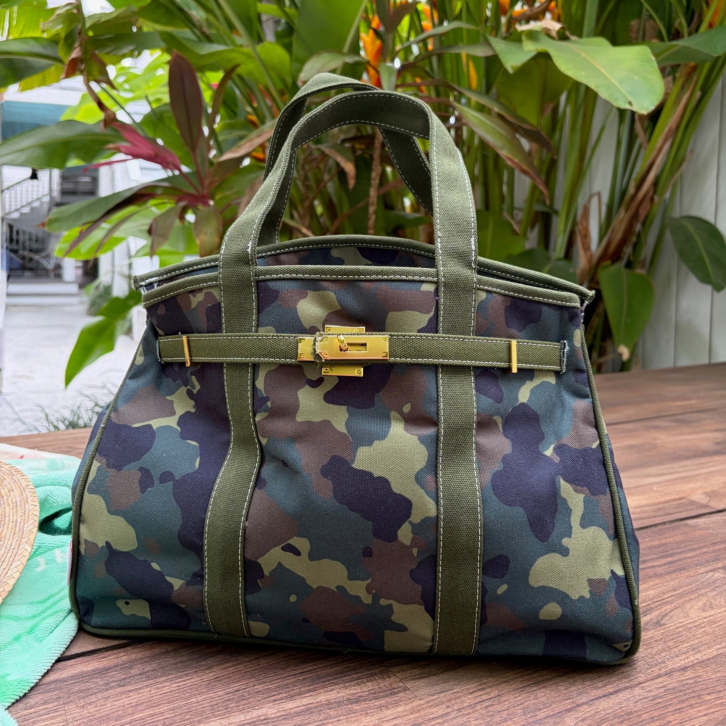 Camouflage Boatkin patterned handbag with green straps on a wooden surface with plants in the background