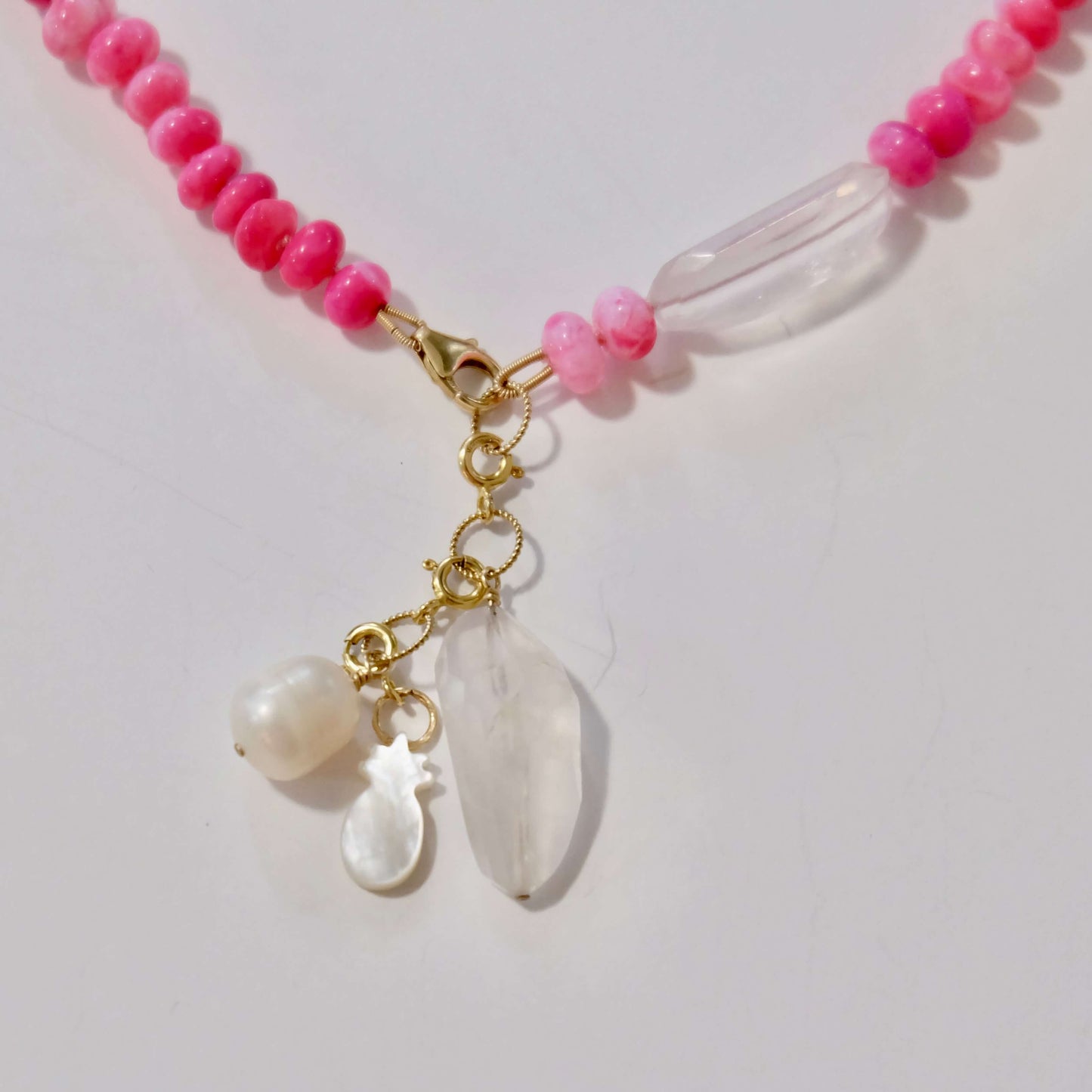 Necklace with pink beads and white shell charms on a light gray background
