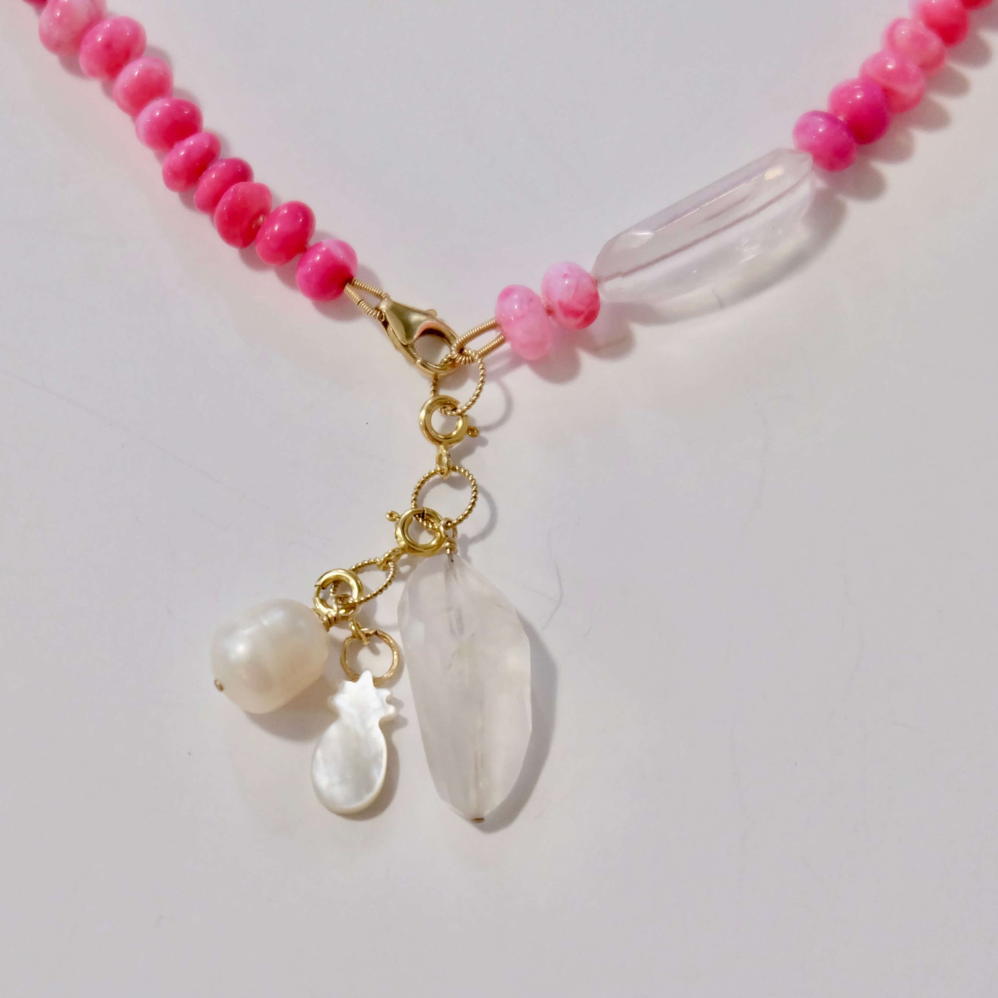 Necklace with pink beads and white shell charms on a light gray background