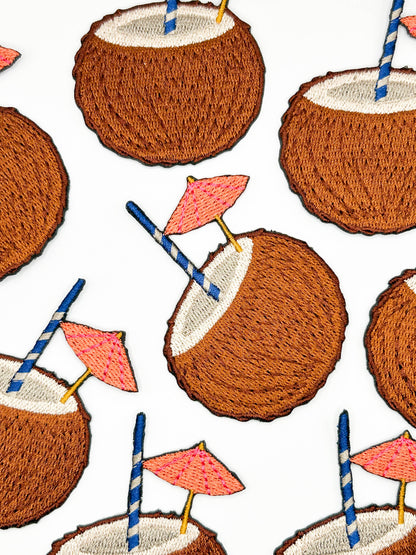 Coconut drink patch with blue striped straw and pink cocktail umbrella