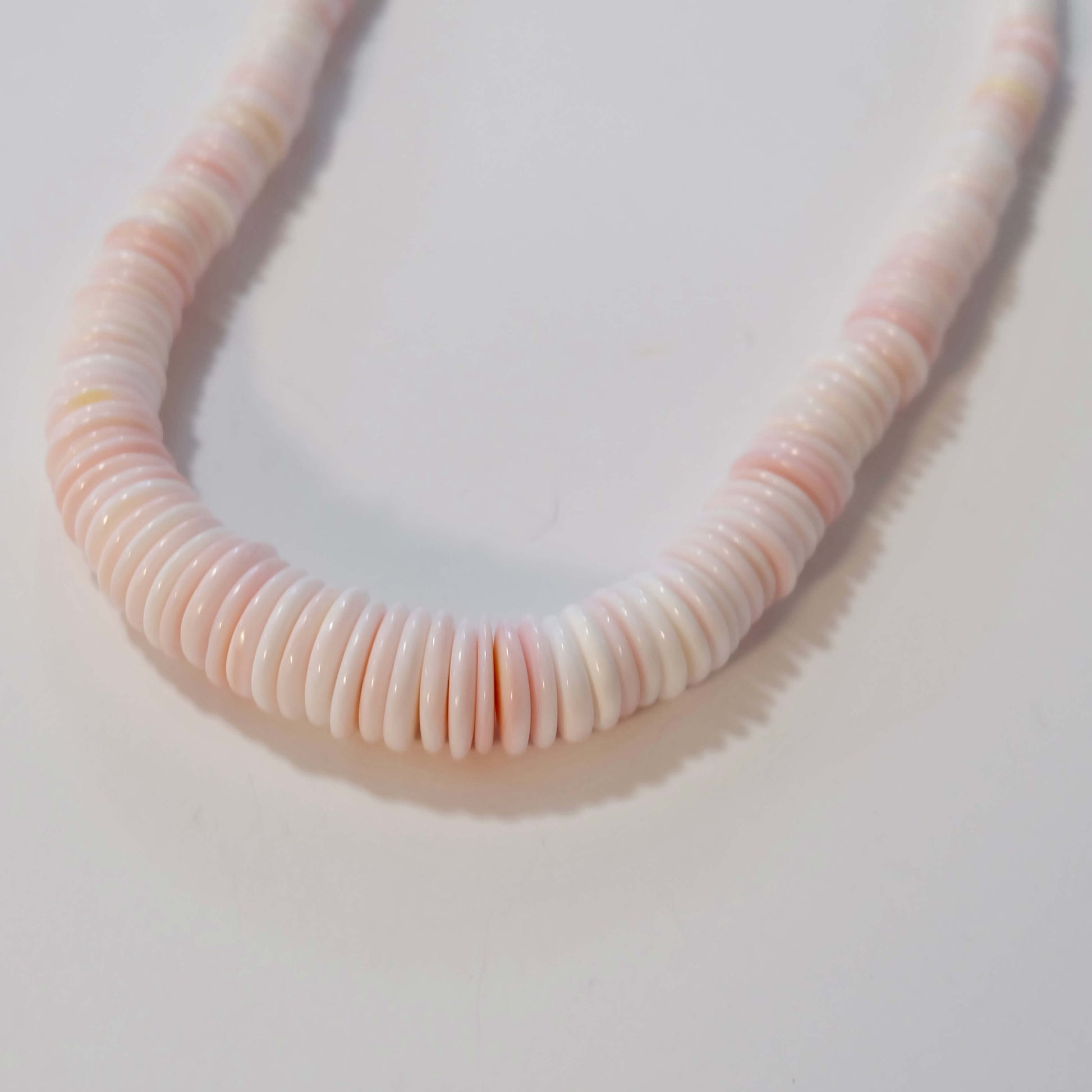Conch shell necklace with pink and white beads on a light gray background