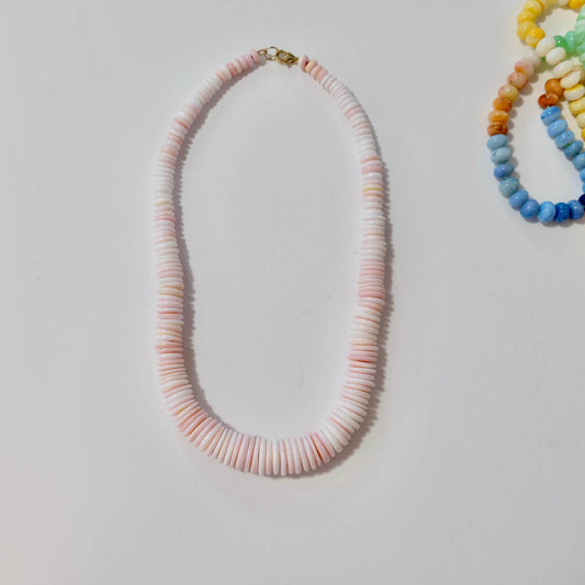 Conch shell necklace with pink and white beads on a light gray background