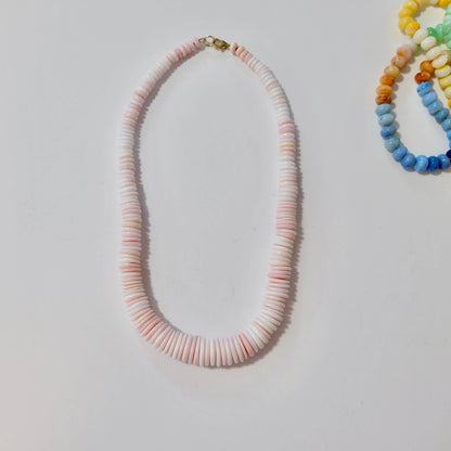 Conch shell necklace with pink and white beads on a light gray background