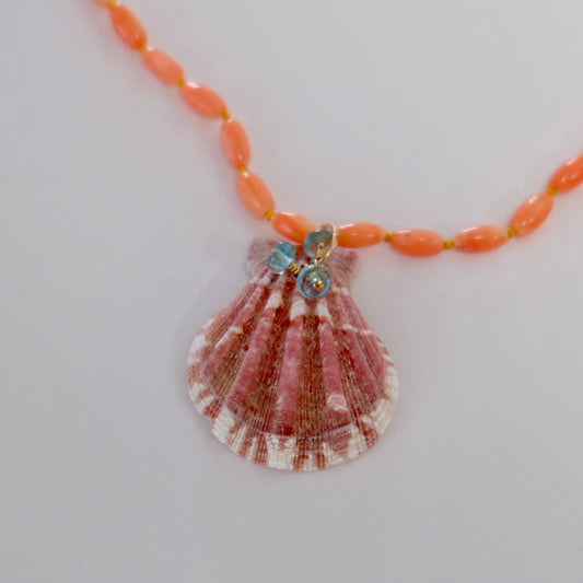 Close-up view of coral necklace with shell and apatite charms on a hand-tied yellow thread necklace.