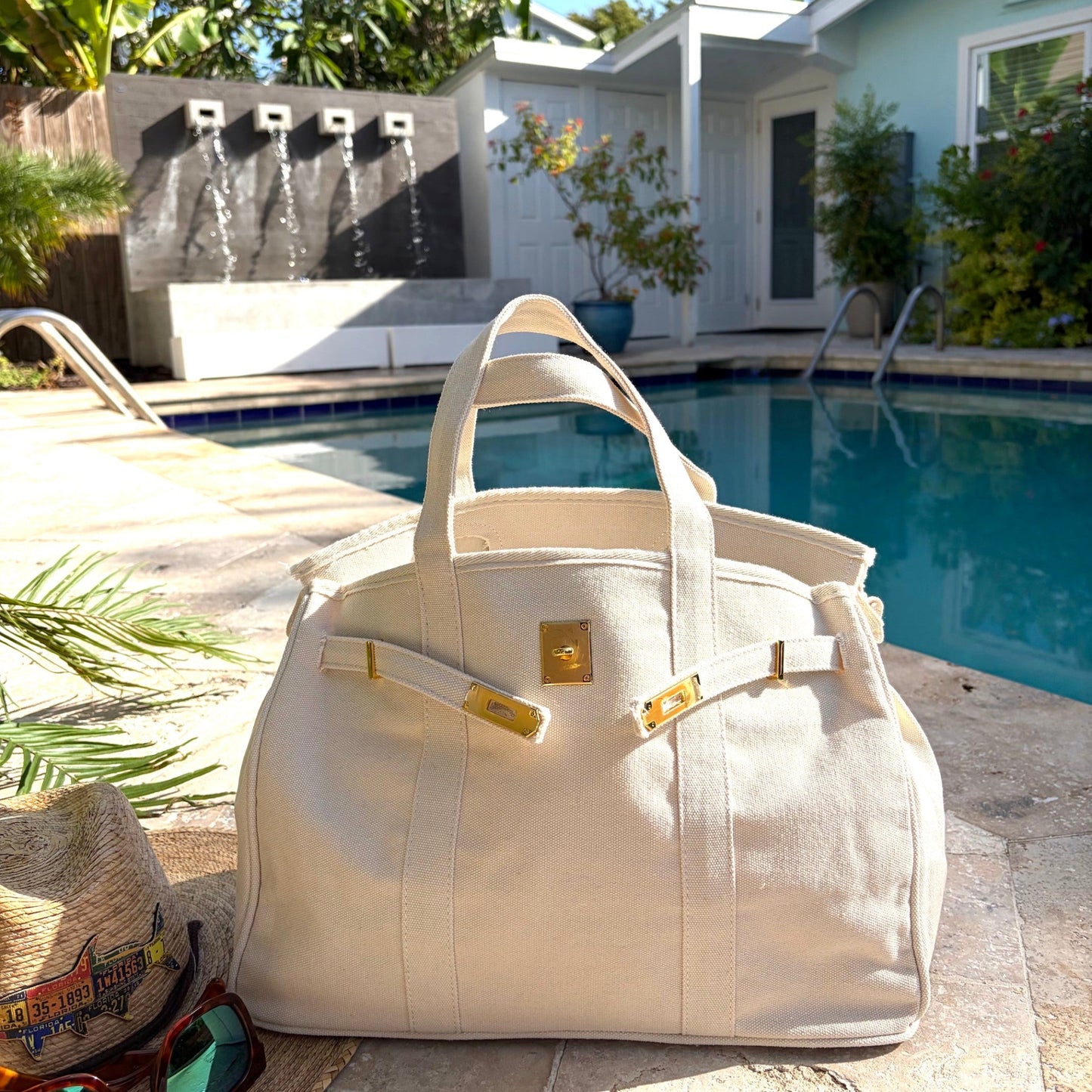 Cream Boatkin bag with gold accents on a patio by a pool.