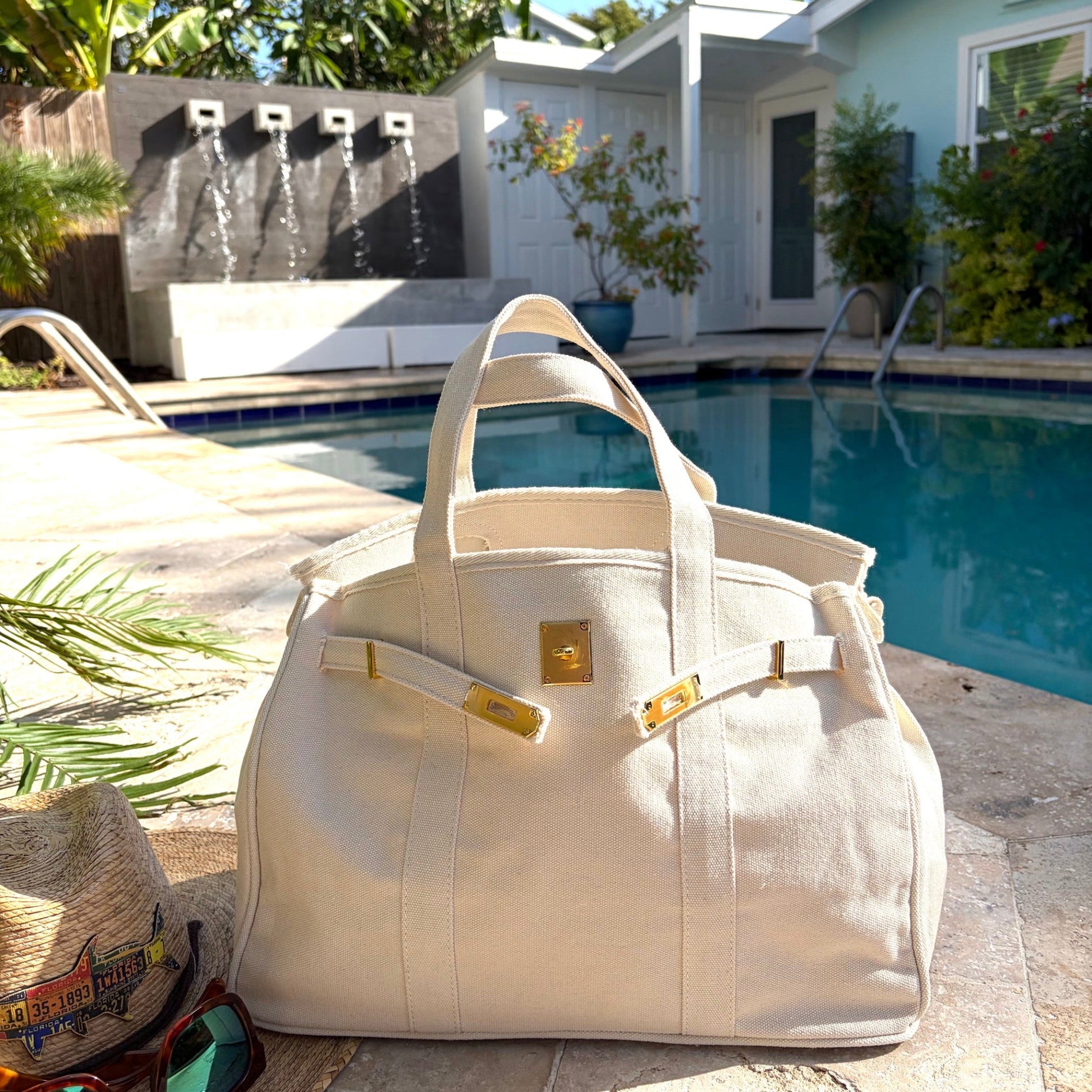 Cream Boatkin bag with gold accents on a patio by a pool.