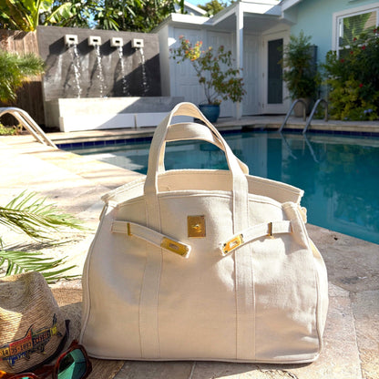 Cream Boatkin bag with gold accents on a patio by a pool.