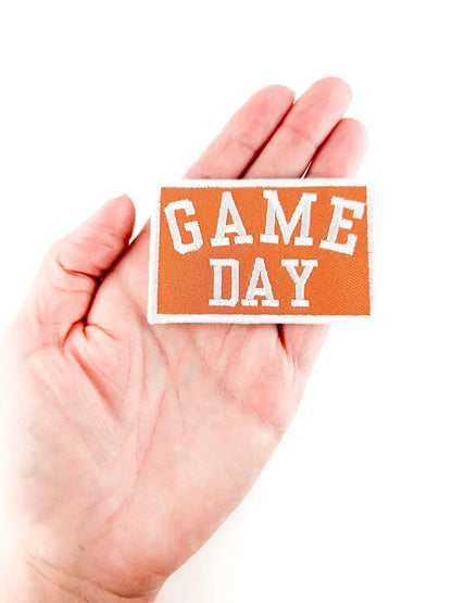 Hand holding a 'GAME DAY' sign with an orange background