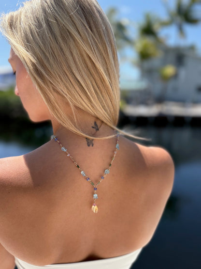 A woman models a vibrant gemstone lariat necklace, showcasing its colorful stones against her outfit.