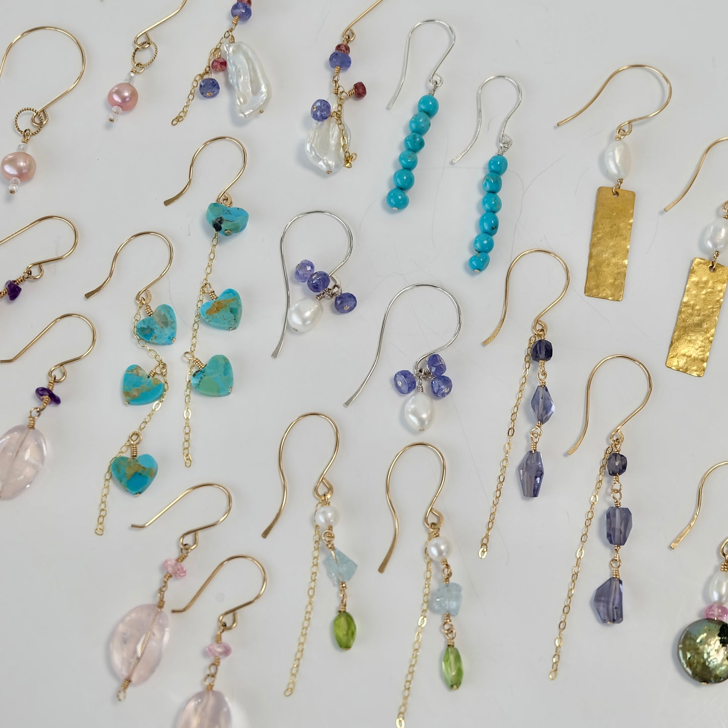 Collection of gold gemstone dangle earrings with different designs and colors on a light background
