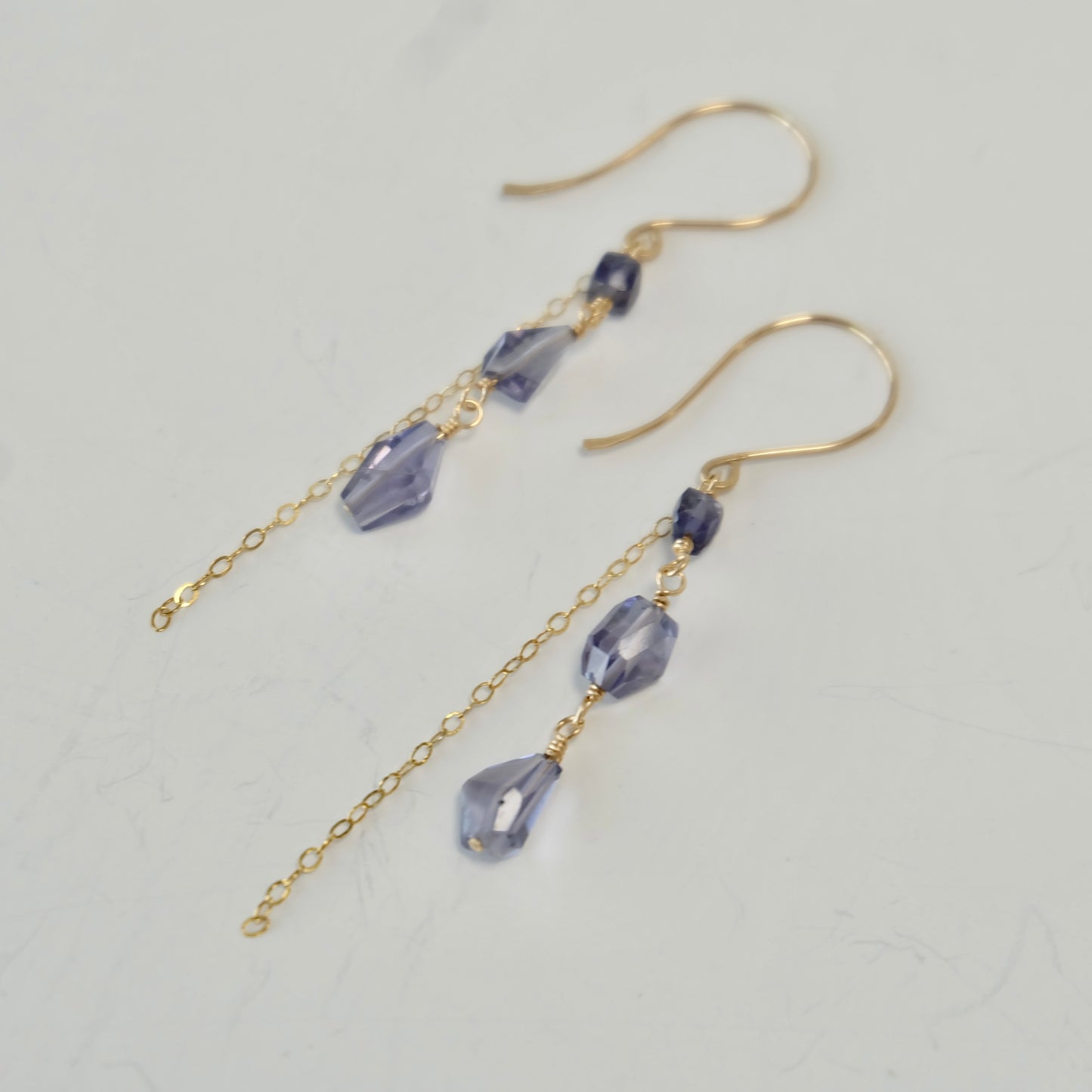 Close up of gold iolite gemstone dangle earrings with purple beads on a light gray background